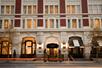 The front entrance of the Hotel Teatro with small trees along the sidewalk and the rows of windows glowing with light/