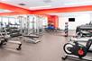 A modern fitness center with red walls, a weights area with a mirror wall to the left, and a cardio area to the right.