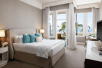 One king bed, bedside lamps, seating area, TV, balcony, and ocean view in a guest room.