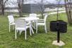 An outdoor picnic area with a white plastic table and chairs next to a small barbecue at Howard Johnson by Wyndham New Braunfels.