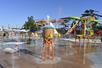 An empty colorful children's splash pad play area with water slides in the background on a sunny day.