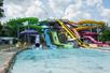 A line of six waterslides in rainbow order purple to red left to right all leading to a small splash pool on a sunny day.