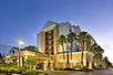 Front exterior of the Hyatt Place Orlando with palm trees lining the sides and the walkways with the sun setting in the background.