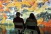 Two people sitting next to each other in dark room observing at a wall fully projected with Van Gogh's famous painting at the Immersive Van Gogh Las Vegas.