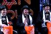 Three men wearing hats and playing the drums on upside down orange buckets on stage at the Jew Man Group Comedy Show.