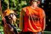 A woman getting ready to zip line with assistance from a crew member in an orange shirt at Jungle Zipline Maui.