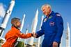 A young boy in an orange astronaut jumpsuit shaking hands with one of the astronauts from Kennedy Space Center.