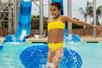 A young girl in a yellow swim suit dragging a blue tube through the water at Knott's Soak City Water Park in Los Angeles, California.