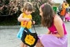 A joyful moment between a young girl in a colorful outfit and a woman, as the girl examines a Halloween-themed bag with a pumpkin design at LEGOLAND California.