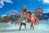 Children joyfully splashing water and playfully interacting in a vibrant water park, surrounded by colorful slides and attractions under a clear blue sky.