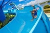 Two children joyfully sliding down a bright blue water slide, surrounded by a sunny atmosphere and lush greenery.