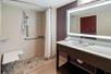 A large bathroom with purple walls, an accessible walk-in shower with a bench, and a vanity with a lit mirror over it.