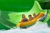 A mother and two children are enjoying a thrilling ride on a green water slide together in a yellow raft, sliding down into the rushing waters at Idlewood.