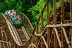 A group of people enjoying a ride on a wooden roller coaster amidst lush greenery at Idlewood.