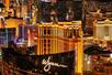 Aerial view of a Maverick helicopter flying over the Las Vegas strip at night with golden hotel lights illuminating the city.