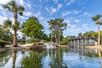 Scenic pond with waterfall and man-made bridge with palm trees around it and a blue sky overhead.