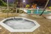 A octagonal bubbling hot tub with a large swimming pool featuring a rock wall in the background.