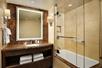 A modern bathroom with a brown vanity with a lit mirror and to the right of it a shower and tub combo with glass sliding doors.