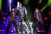 A Michael Jackson impersonator performing on stage wearing a black sequined jacket and black pants surrounded by backup dancers.