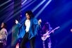 Michael Knight sings on stage as Michael Jackson, wearing a blue long sleeve with white shirt underneath and black pants along with his band on the background at Reza Live Theatre in Branson, Missouri.