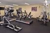 A small fitness center with several pieces of cardio equipment throughout the room and a mirror wall on the left side.