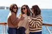 Three women in sunglasses standing together holding their drinks up and smiling on the Marina del Rey Brunch Cruise.