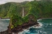 a tendril-like rock formation coming into the ocean and a waterfall flowing into the ocean seem from just above the ocean on Maui's Hana & Haleakala Helicopter Tour in Hawaii USA.