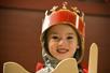 A child is dressed up with a crown, sword, and shield