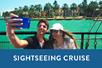 Young couple taking a selfie with blue water behind them and a box saying "Sightseeing Cruise' with Miami Aqua Tours in Miami, Florida, USA.