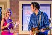 A Carl Perkins impersonator playing guitar on stage with a woman in a pink dress playing tambourine at the Million Dollar Quartet.