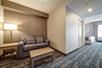 A hotel room living area with a sofa bed, wooden coffee table, side table, and lamp with the bedroom to the right.