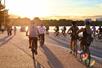 A large group of tourist riding bikes near water with a bright light orange sunset shining in front of them in Washington DC.