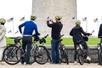 A group of tourist wearing green helmets standing with their bikes and taking pictures of the Washington Monument in front of them.