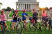 A group of tourist wearing red helmets standing over their bikes with the busy Lincoln Memorial in the background at sunset.