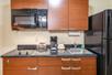 A kitchenette with brown cabinets, a small stove, sink, coffee machine, microwave, and a black refrigerator.