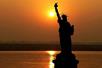 The silhouette of the Statue of Liberty with a bright orange sun setting behind it on the NYC Skyline Sunset Cruise.