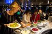 Three people making salads at an open salad bar with a dark dining room full of tables behind them on the New Jersey Dinner Cruise.