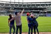 Two couples standing near the grass at the Citi Field Baseball Park point up at the stands on the Citi Field Tour.
