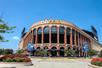 The front exterior of Citi Field Baseball Park with their logo at the top of the building and landscaping around it on a sunny day.