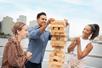 Friends laughing and playing Jenga on a sunny day on the New York Signature Lunch Cruise with the city in the background.