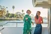 Two women smiling and holding drinks standing on the desk of the Newport Beach Brunch Cruise with the sun shining behind them.