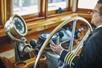 A ship captain in a suit turning a giant gold steering wheel in the bridge of the Newport Beach Brunch Cruise.