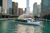 The Odyssey vessel cruising along the Chicago River with the city in the background with the sun starting to set.
