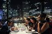 A group of friends seated at a white table enjoying their dinner with a large window showing the city of Chicago at night behind them.
