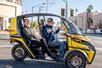 A man and woman in a two-seater doorless yellow GoCar smiling and having a good time on a sunny day in Las Vegas.