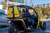 View of a yellow doorless GoCar with two people sitting in it stopped at a traffic light on the streets of Las Vegas.