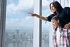 A mother and daughter standing close to a window at the One World Observatory pointing and looking down at New York City.