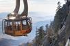 A tramcar full of people in the air in the mountains with the sun shining on it exterior at Palm Springs Aerial Tramway.