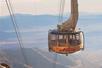 A yellow tramcar with people in it in the air with the mountains in the distance it at Palm Springs Aerial Tramway.