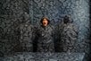 A woman wearing a shocked expression stands alongside two others, all clad in full-body camouflage coats designed to match the room's exact pattern and color, creating a mesmerizing visual illusion at Paradox Museum Las Vegas, NV
